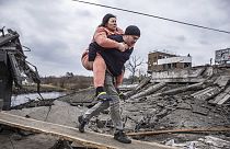 Un hombre lleva a una mujer mientras cruzan un camino improvisado mientras huyen de la ciudad de IrpÍn, Ucrania, el domingo 6 de marzo de 2022