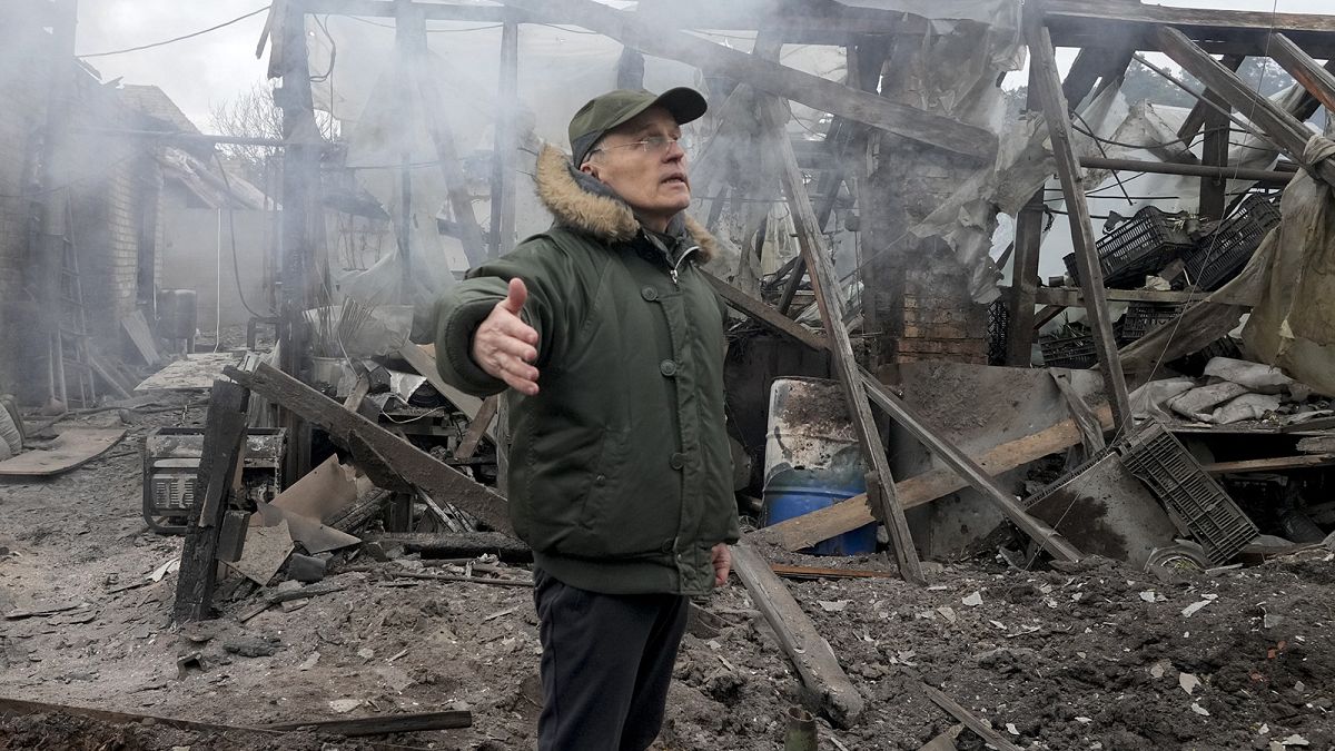 A man opens his arms as he stands near a house destroyed in the Russian artillery shelling, in the village of Horenka close to Kyiv