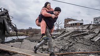 A man carries a woman as they cross an improvised path while fleeing the town of Irpin, Ukraine, Sunday, March 6, 2022. 