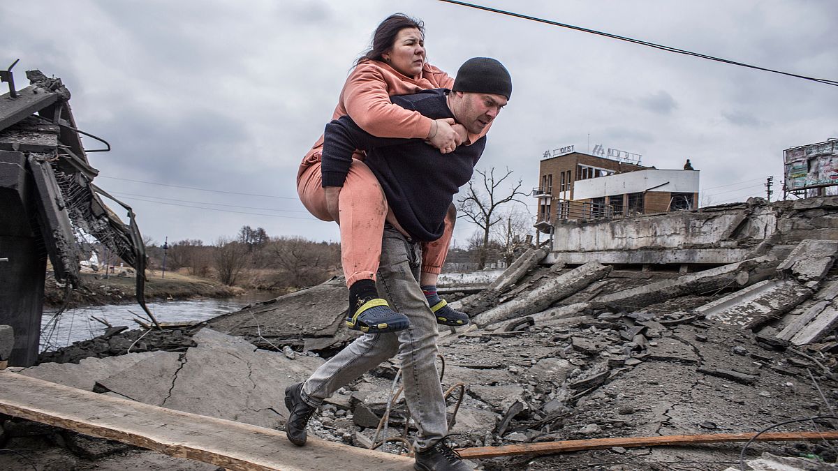 Egy férfi visz a hátán egy nőt menekülés közben, egy rögtönzött ösvényen kelnek át az ukrajnai Irpin városából, 2022. március 6-án, vasárnap. 