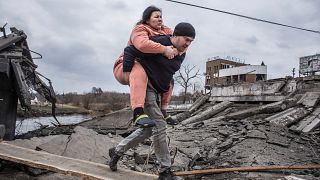 Egy férfi visz a hátán egy nőt menekülés közben, egy rögtönzött ösvényen kelnek át az ukrajnai Irpin városából, 2022. március 6-án, vasárnap.
