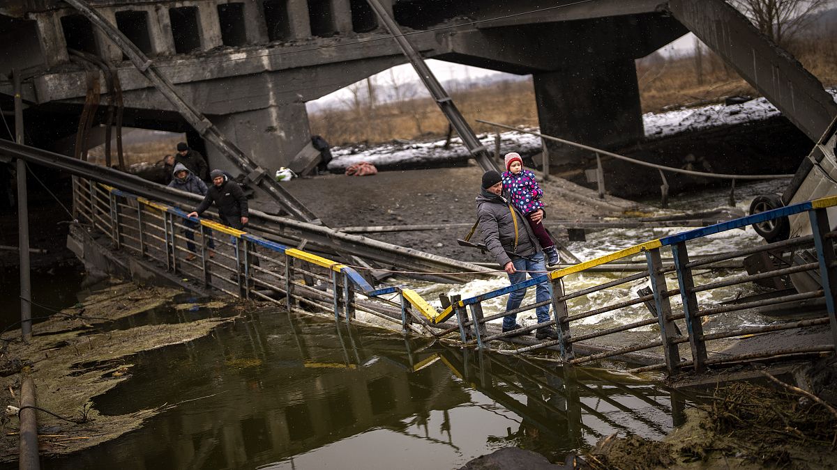 Local militiaman Valery, 37, carries a child as he helps a fleeing family across a bridge destroyed by artillery, on the outskirts of Kyiv, Ukraine, Wednesday, March 2. 2022