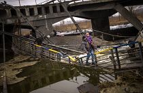 Local militiaman Valery, 37, carries a child as he helps a fleeing family across a bridge destroyed by artillery, on the outskirts of Kyiv, Ukraine, Wednesday, March 2. 2022