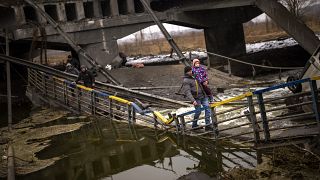 Local militiaman Valery, 37, carries a child as he helps a fleeing family across a bridge destroyed by artillery, on the outskirts of Kyiv, Ukraine, Wednesday, March 2. 2022