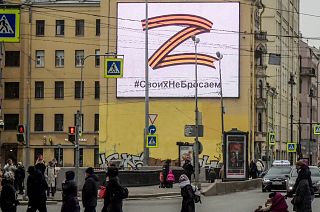 Pedestrians cross a street in front of a billboard displaying the symbol Z in the colours of the ribbon of Saint George and a slogan reading: "We don't give up on our people".