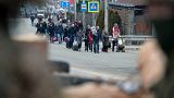 People carrying baggage after crossing the bombed-out bridge, soldiers in foreground.