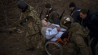 Des soldats ukrainiens portent une femme en fauteuil roulant, tandis que des personnes fuient Irpin près de Kiev, le 07/03/2022