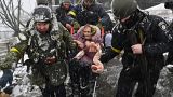 Ukrainian soldiers help an elderly woman to cross a destroyed bridge as she evacuates the city of Irpin, northwest of Kyiv, on March 8, 2022.