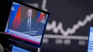 Russia's President Vladimir Putin appears on a television screen at the stock market in Frankfurt, Germany, Feb. 25, 2022. Russia is revving up its propaganda machine.