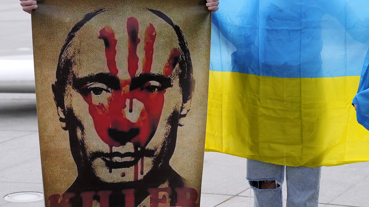 متظاهر يحمل لافتة تظهر الرئيس الروسي فلاديمير بوتين آخر يحمل العلم الأوكراني خلال مظاهرة في نيقوسيا، قبرص.