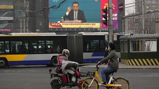 People ride past a large video screen showing Chinese Premier Li Keqiang after the closing session of China's National People's Congress in Beijing.
