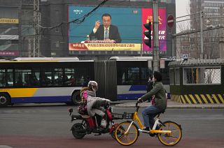People ride past a large video screen showing Chinese Premier Li Keqiang after the closing session of China's National People's Congress in Beijing.