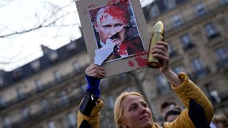متظاهرة أوروبية ترفع ملصقاً يشبه بوتين بهتلر
