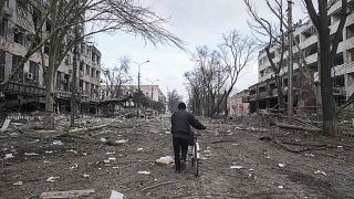 A man walks with a bicycle in a street damaged by shelling in Mariupol, Ukraine, Thursday, March 10, 2022