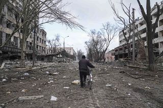 A man walks with a bicycle in a street damaged by shelling in Mariupol, Ukraine, Thursday, March 10, 2022