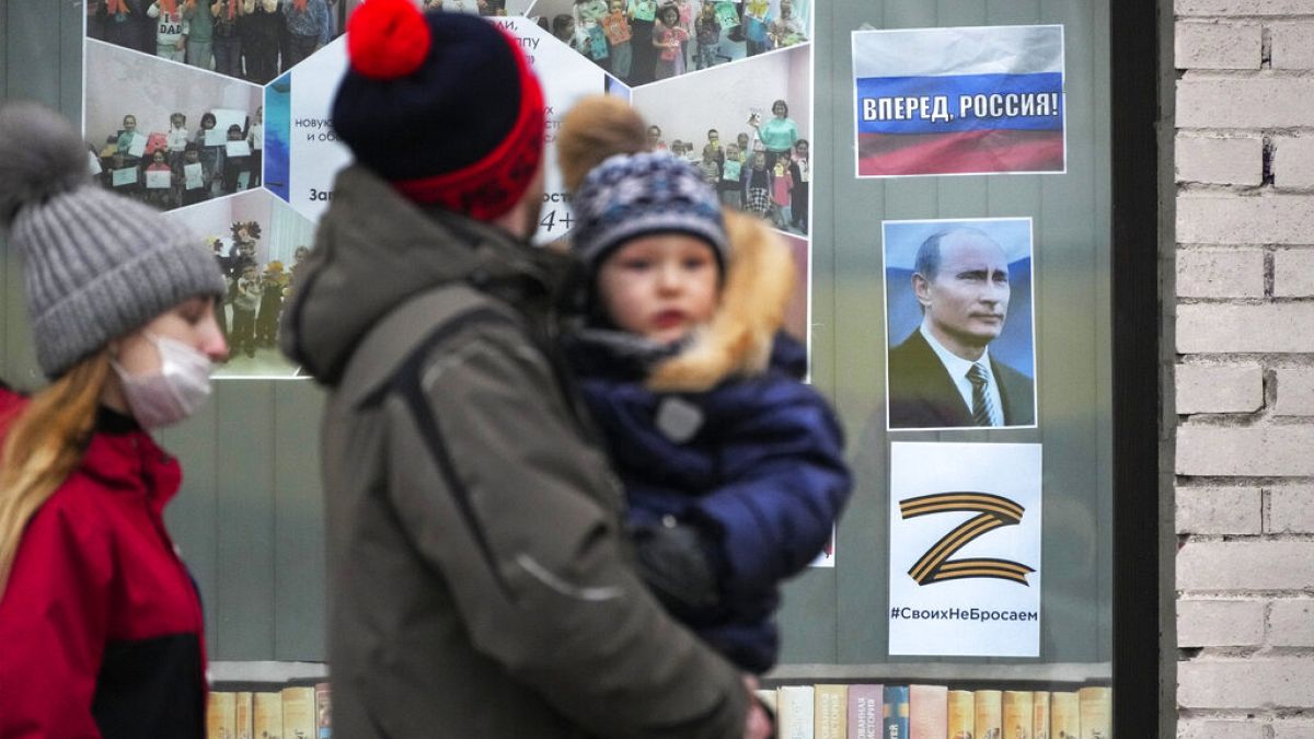 Egy család sétál el Szentpéterváron a gyermekkönyvtár előtt, ahol Putyin elnök portréja és az ukrán hoború szimbólumává vált Z betűt tettek a kirakatba
