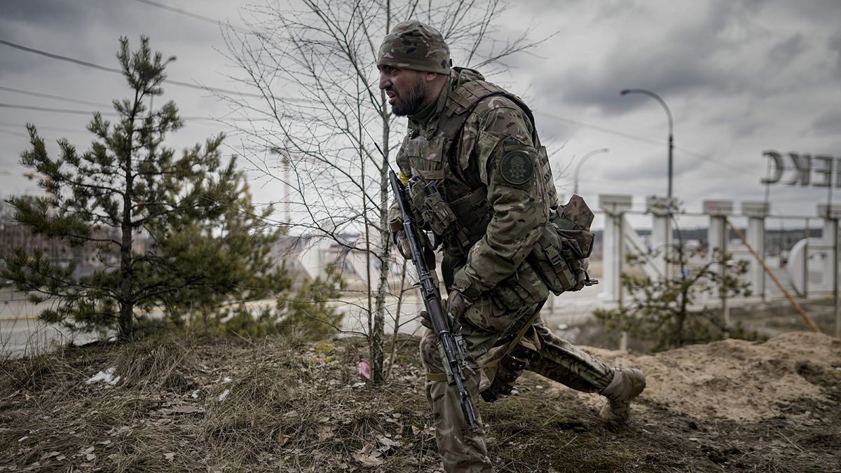 A Ukrainian serviceman takes a shooting position as he looks at approaching vehicles in Irpin, on the outskirts of Kyiv