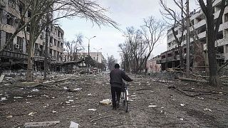 A man walks with a bicycle in a street damaged by shelling in Mariupol