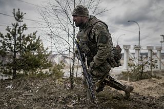 A Ukrainian serviceman takes a shooting position as he looks at approaching vehicles in Irpin, on the outskirts of Kyiv