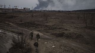 Soldiers walk on a path as smoke billows from the town of Irpin, on the outskirts of Kyiv on Saturday