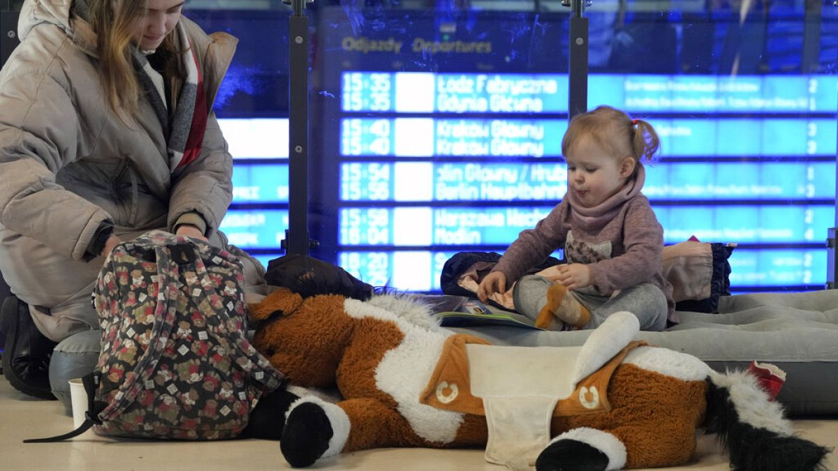 Une jeune femme joue avec une petite fille assise sur un matelas gonflable dans la gare de Varsovie, le 13 mars 2022