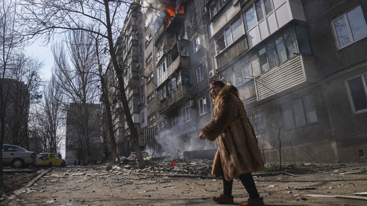 A woman walks past a burning apartment building after shelling in Mariupol