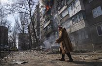 A woman walks past a burning apartment building after shelling in Mariupol