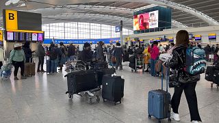 Passengers queue to check in, at Heathrow Airport in London.
