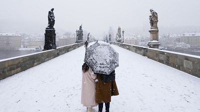 A couple crosses the medieval Charles Bridge as snow falls in Prague, Czech Republic, Friday, March 4, 2022.
