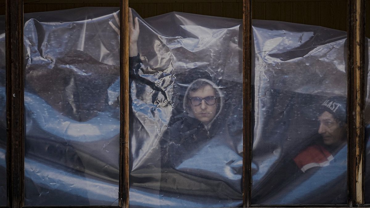 People put up plastic sheets to cover the broken windows of their apartments after parts of a Russian missile landed on an apartment block in Kyiv on 17 March 2022