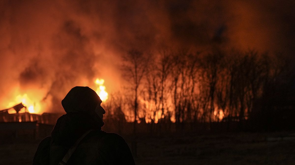 A Ukrainian serviceman is backdropped by a blaze at a warehouse after a bombing on the outskirts of Kyiv, Ukraine, Thursday, March 17, 2022.