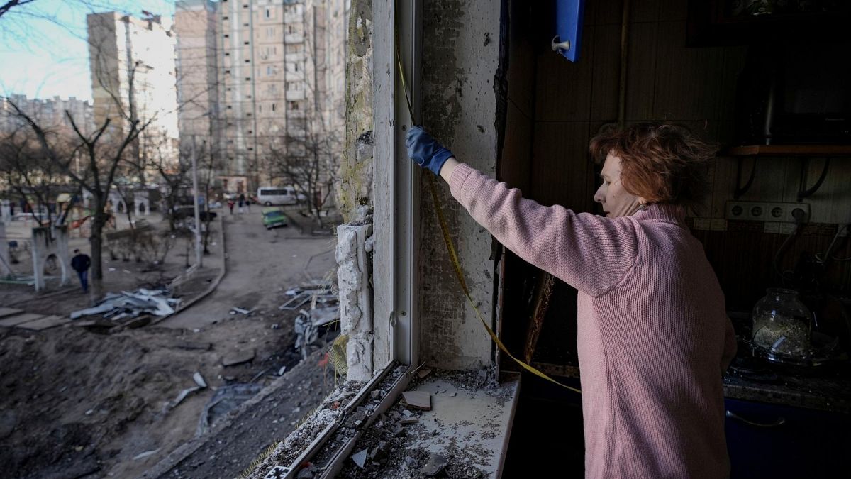 A woman measures a window before covering it with plastic sheets in a building damaged by a bombing the previous day in Kyiv, Ukraine, Monday, March 21, 2022. 