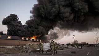 Ukrainian servicemen carry containers backdropped by a blaze at a warehouse after a bombing on the outskirts of Kyiv, 17 March 2022