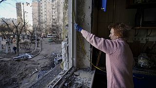 Une femme mesure une fenêtre avant de la recouvrir de feuilles de plastique dans un bâtiment endommagé par un bombardement la veille à Kiev, en Ukraine, lundi 21 mars 2022
