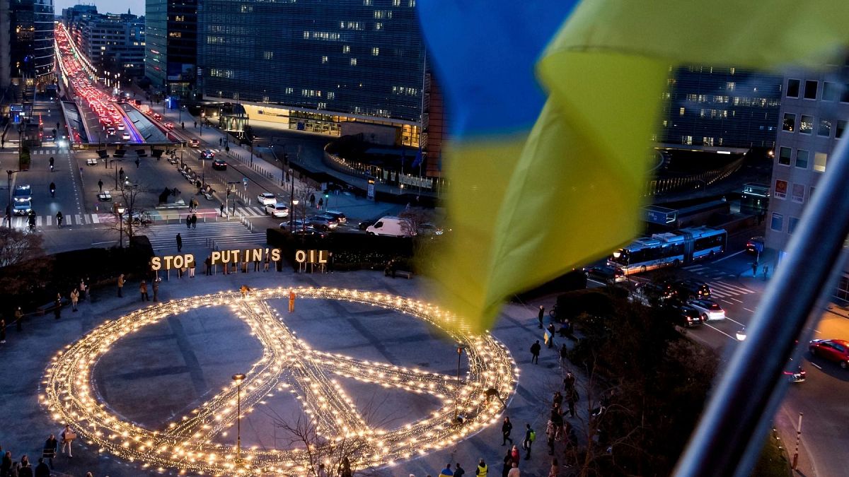 People stand around a giant peace sign with the message 'Stop Putin's Oil', put up by demonstrators ahead of an EU and NATO summit in Brussels, Tuesday, March 22, 2022.