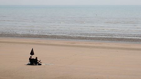 Two sunbathers sit and watch the sea on the sandy beach at Camber Sands, England.