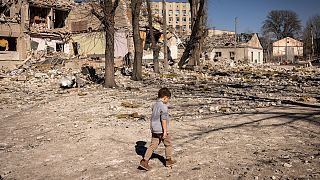 Egy kisgyerek sétál egy megrongálódott iskola előtt Zsitomirban 2022. március 23-án
