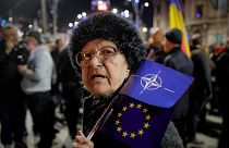 یکی از معترضان به حمله روسیه پرچم‌های ناتو و اتحادیه اروپا در رومانی را در دست دارد