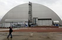  A man walks past a shelter covering the exploded reactor at the Chernobyl nuclear plant, in Chernobyl, Ukraine, Thursday, April 15, 2021. 