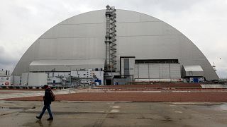  A man walks past a shelter covering the exploded reactor at the Chernobyl nuclear plant, in Chernobyl, Ukraine, Thursday, April 15, 2021. 