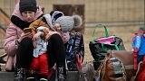 A woman with her child checks her mobile phone as she waits for relocation outside the main shelter and relocation center in Przemysl, southeastern Poland.