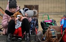 A woman with her child checks her mobile phone as she waits for relocation outside the main shelter and relocation center in Przemysl, southeastern Poland.