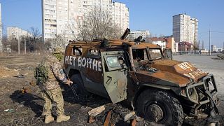 Ukrán katona néz egy megrongálódott orosz katonai járművet Harkivban