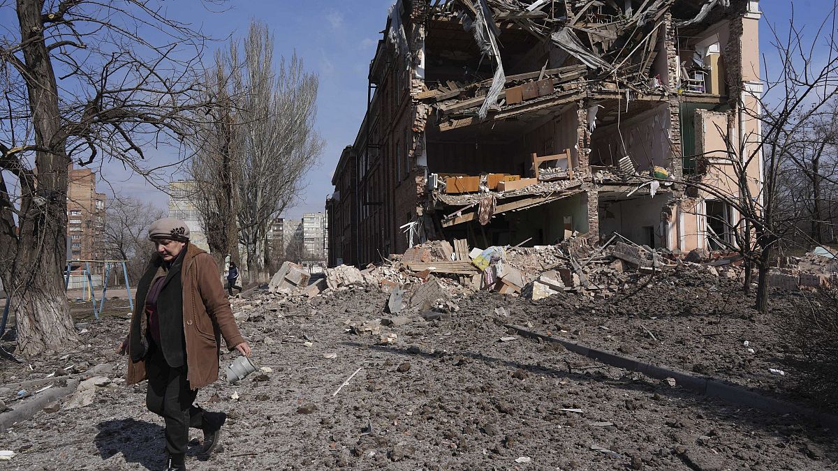 A woman walks past building damaged by shelling in Mariupol, Ukraine, Sunday, March 13, 2022.