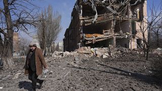 A woman walks past building damaged by shelling in Mariupol, Ukraine, Sunday, March 13, 2022.