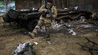 A Ukrainian serviceman kicks a burnt sleeping bag near the wreck of a Russian tank in Stoyanka, Ukraine, Sunday, March 27, 2022