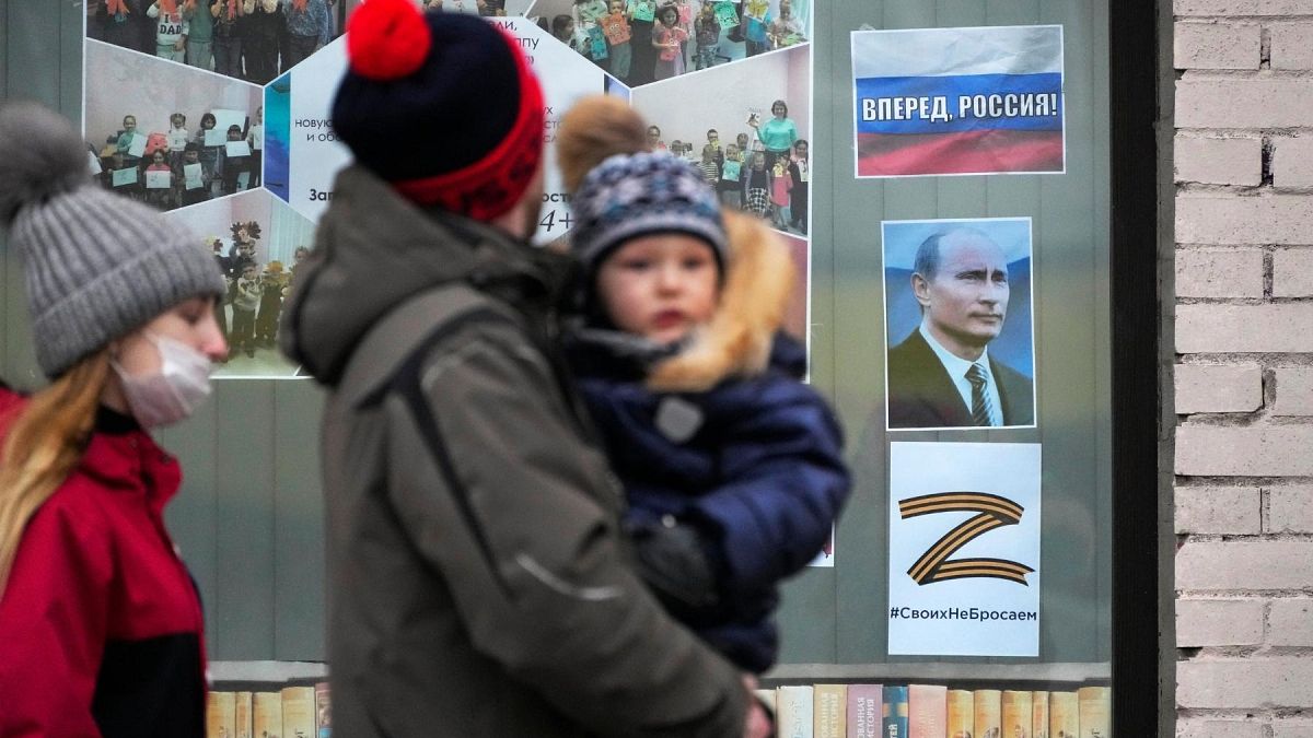 FILE - A family walk past a portrait of Russian President Vladimir Putin, a sign reading 'Go Russia!' St. Petersburg, Russia, Friday, March 11, 2022