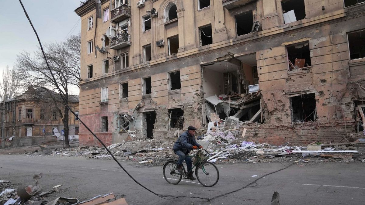 رجل يمر بدراجة هوائية أمام مبنى سكني مدمر في ماريوبول بأوكرانيا.