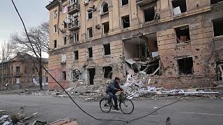 رجل يمر بدراجة هوائية أمام مبنى سكني مدمر في ماريوبول بأوكرانيا.