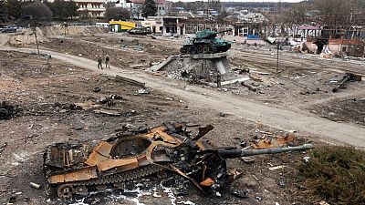 Local residents pass by a damaged Russian tank in the town of Trostyanets.